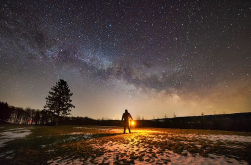 Figure holding a lantern with Milky Way galaxy in background.