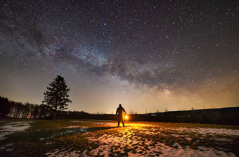 Figure holding a lantern with Milky Way galaxy in background.