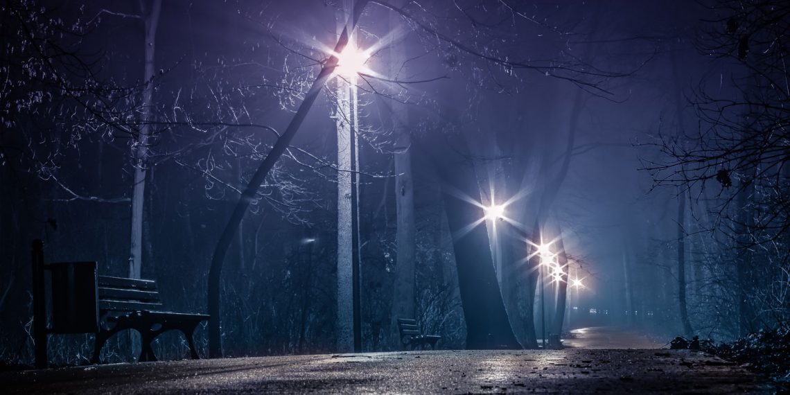 Park lights illuminate the sidewalk on a dark night.