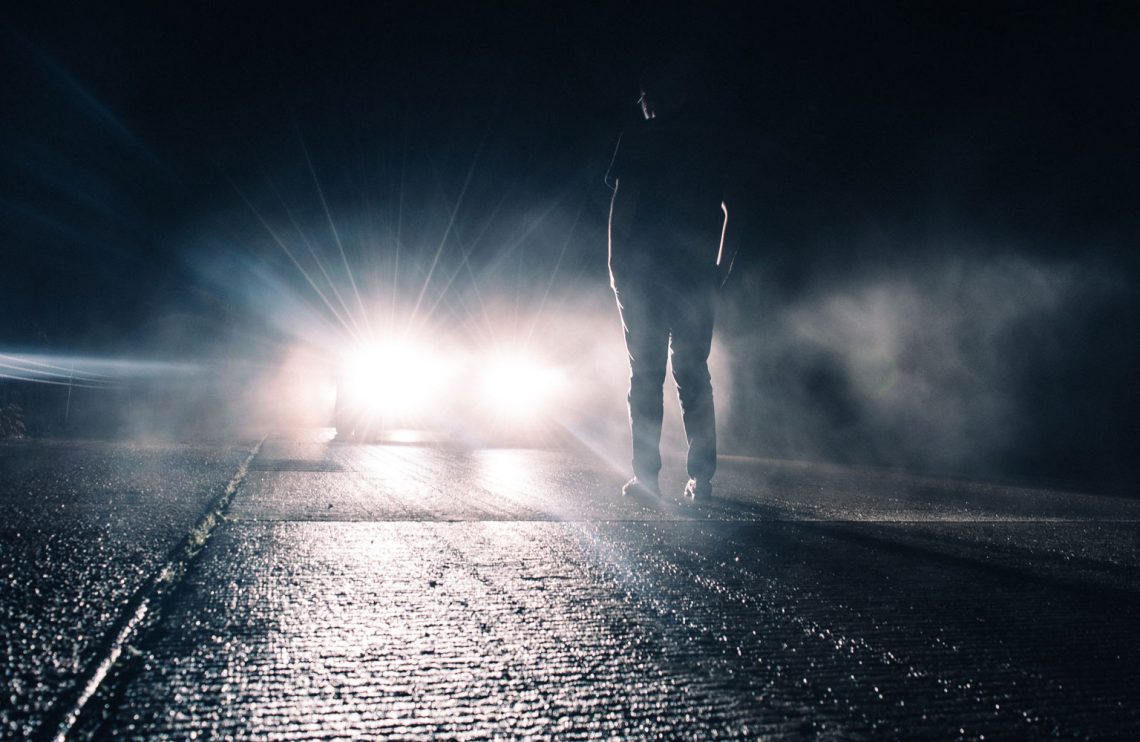 Man standing in front of car headlights.