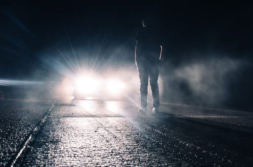 Man standing in front of car headlights.