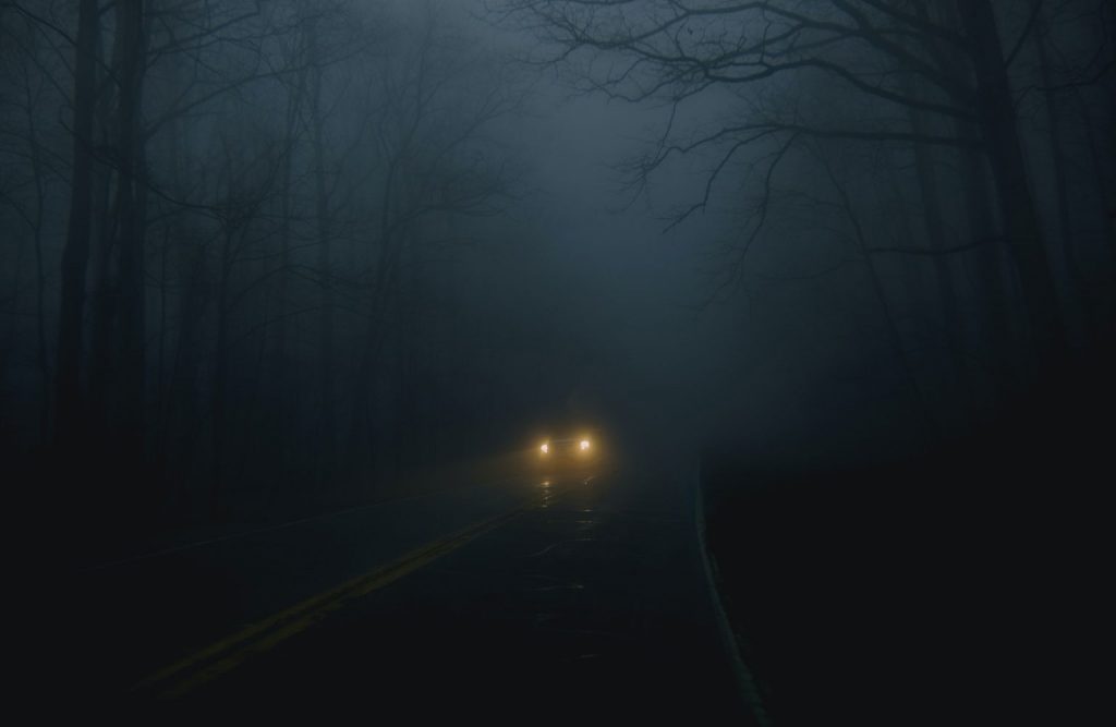 Vehicle headlights are visible on a dark road.