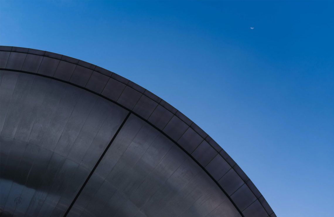 A domed structure with the moon high up in the sky.