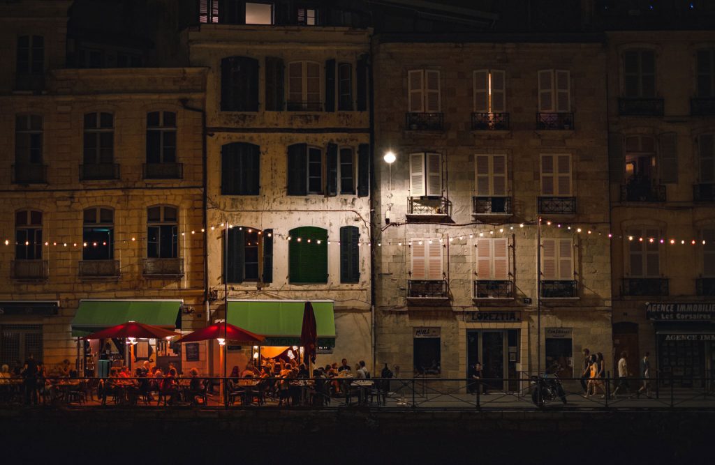 People gathering at a cafe along a row of buildings in France.