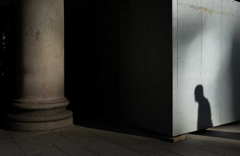 Gray concrete pillar near wall with silhouette of a man next to it.