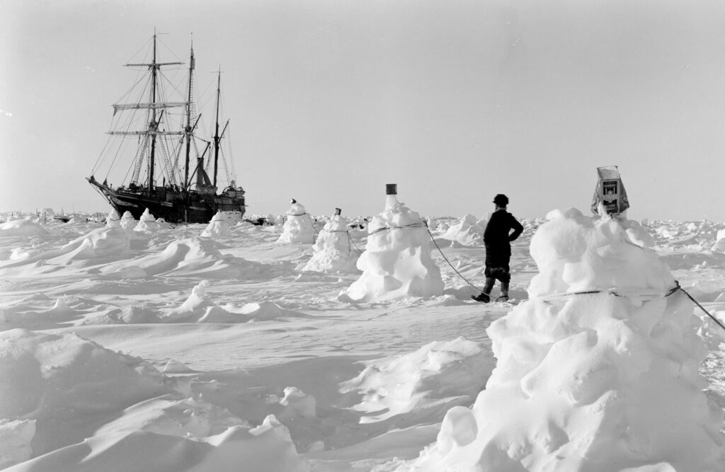 Ship in the distance with a man standing on the ice in Antarctica.