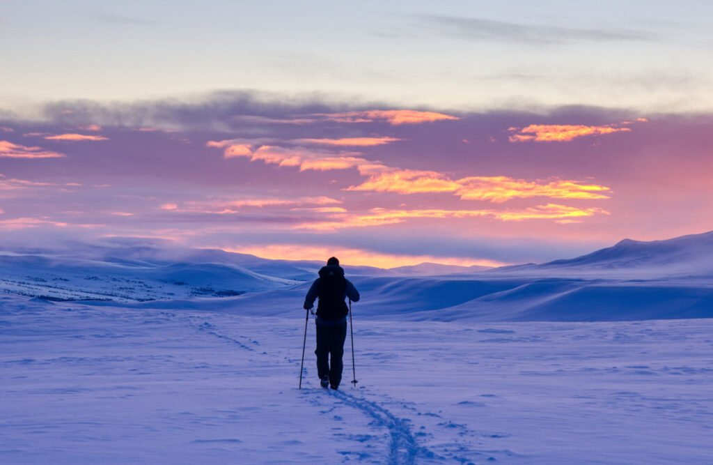 Man hiking on snow covered ground during a sunrise.