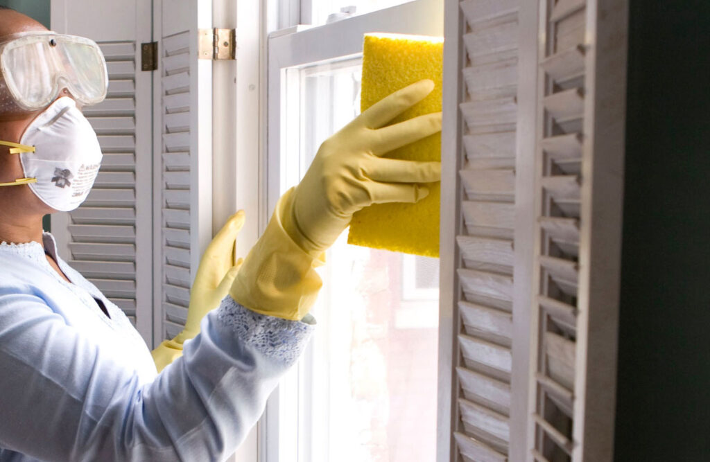 Woman cleaning a window with a sponge and protective gear.