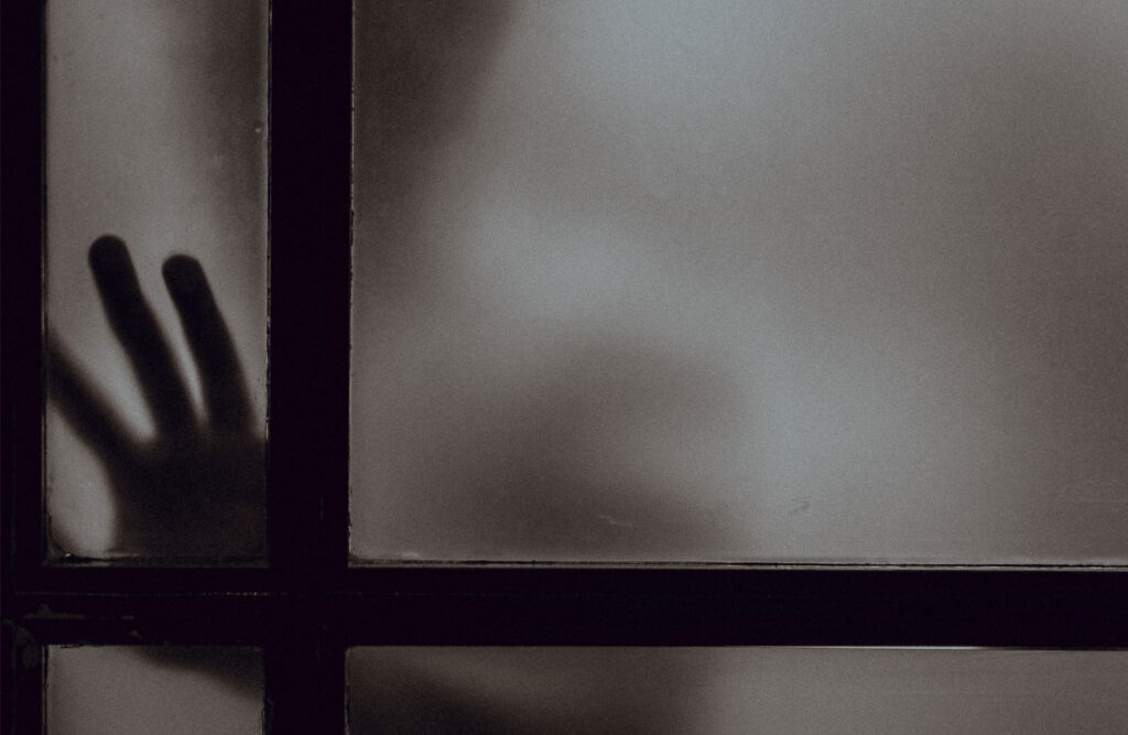 Person touching a frosted glass window that only shows their silhouette.