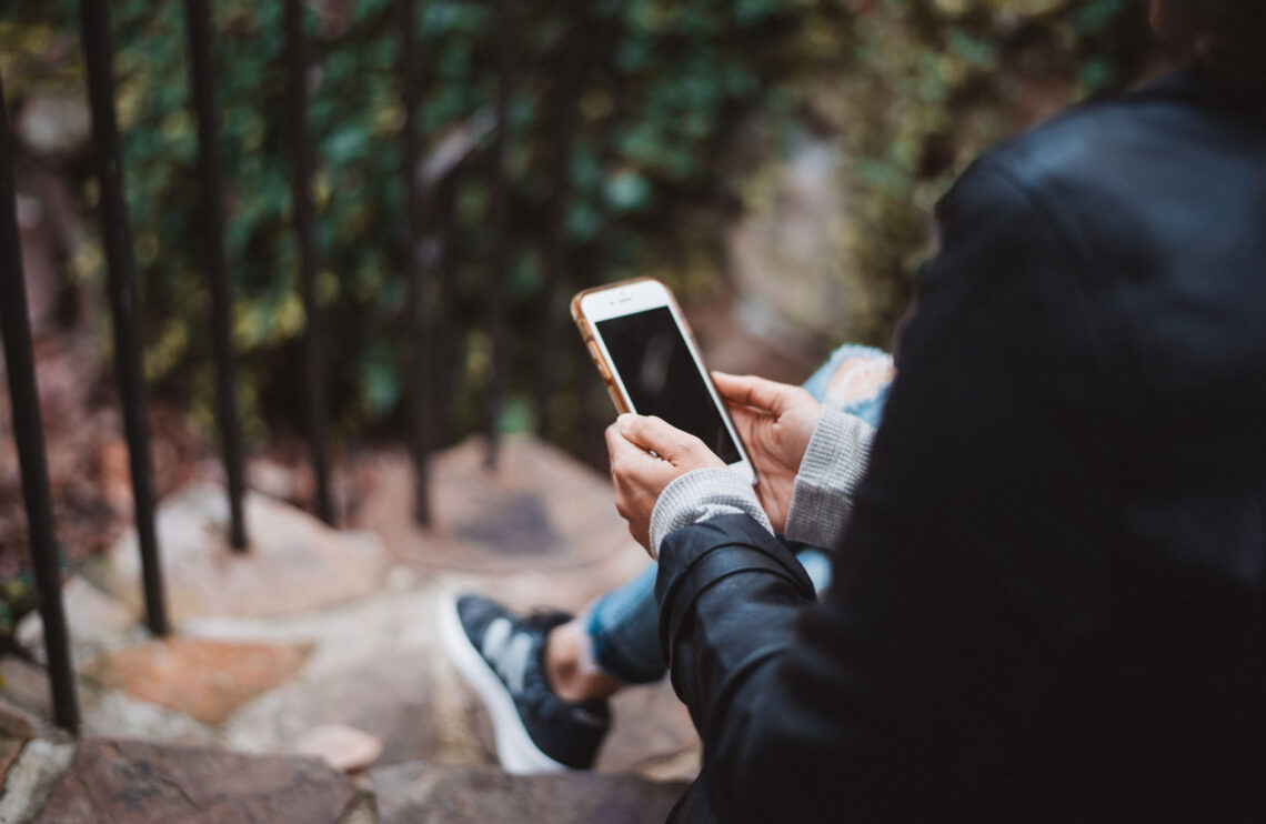 Person holding white smartphone sitting on stairs.